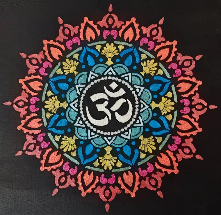 A radial mandala with the Aum (Om) symbol at its centre, ringed by lotus petals in pink, blue, gold, and teal on a black ground.