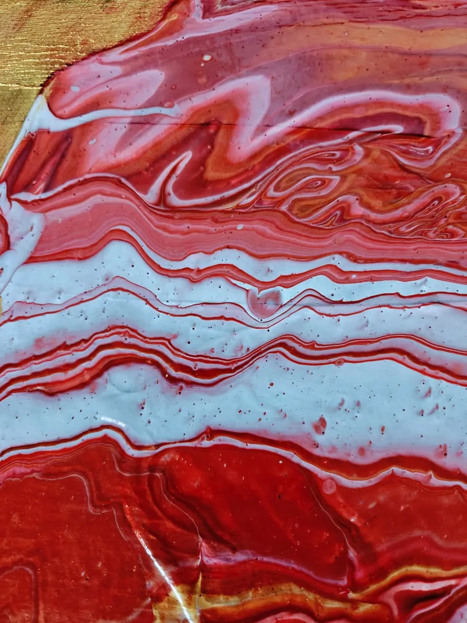 A fluid pour of crimson, coral, and ice-white in horizontal bands with a gold edge, resembling banded carnelian agate.