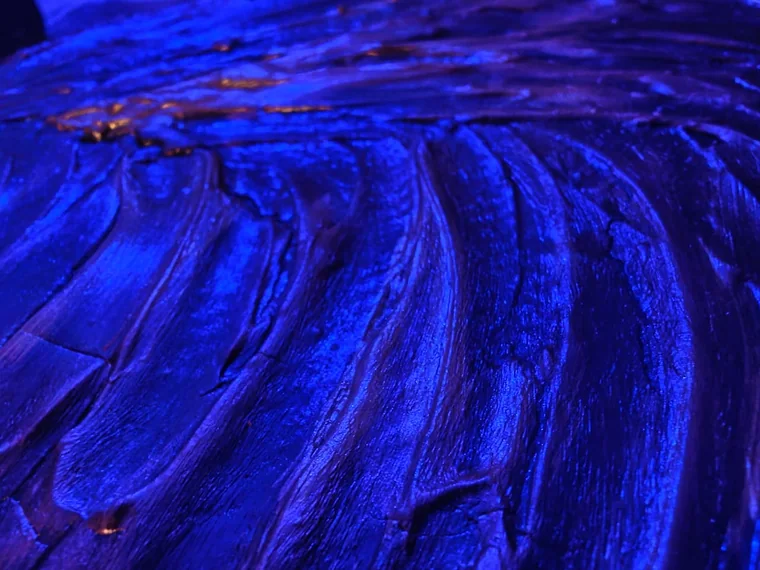 The same swirling sculptural relief lit in deep ultramarine and cobalt blue, the sculpted ridges almost submerged in colour but for a few gold flecks.