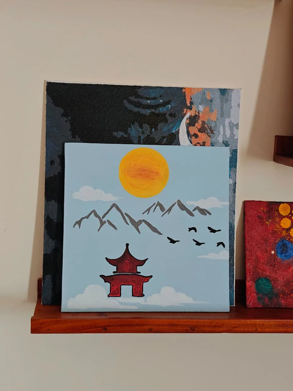 A flat-colour painting of a red pagoda temple resting on a bank of white cloud, with grey mountain peaks, a yellow sun and a skein of dark birds against a pale blue sky.